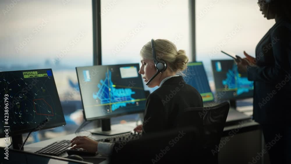 Black Female Air Traffic Controller Holding Tablet in Airport Tower. Office Room is Full of Desktop Computer Displays with Navigation Screens, Airplane Flight Radar Data for the Team. Black Female Air Traffic Controller Holding Tablet in Airport Tower. Office Room is Full of Desktop Computer Displays with Navigation Screens, Airplane Flight Radar Data for the Team.