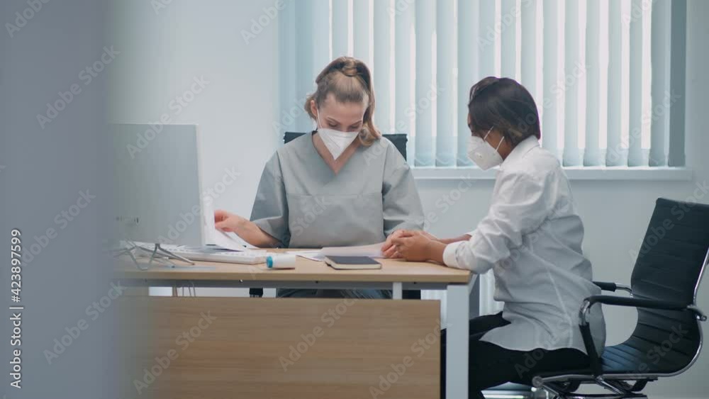 Modern private clinic, dark-skinned female at a doctor's appointment, a doctor female and a young woman in protective medical masks, a doctor's visit during the coronavirus pandemic. Modern private clinic, dark-skinned female at a doctor's appointment, a doctor female and a young woman in protective medical masks, a doctor's visit during the coronavirus pandemic.