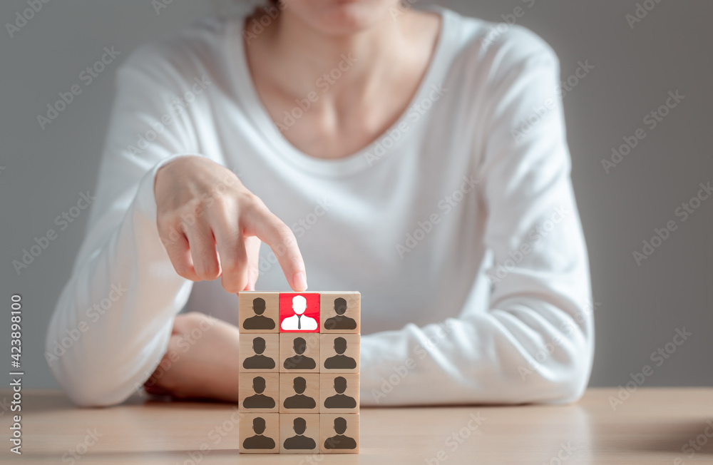 Woman pointing at a wooden block one leader person represented by icon. Leader stands out from crowd, Human resources and corporate hierarchy, recruiter complete team, HR, HRM, HRD concepts. Woman pointing at a wooden block one leader person represented by icon. Leader stands out from crowd, Human resources and corporate hierarchy, recruiter complete team, HR, HRM, HRD concepts.