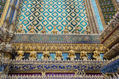 Beautiful traditional mosaic decor with gold details and statues at wall of Temple of Emerald Buddha. Grand Palace complex, Bangkok, Thailand