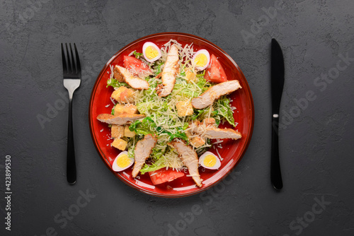 Red plate of Caesar Salad over black background. Traditional Italian cuisine concept, traditional recipe.