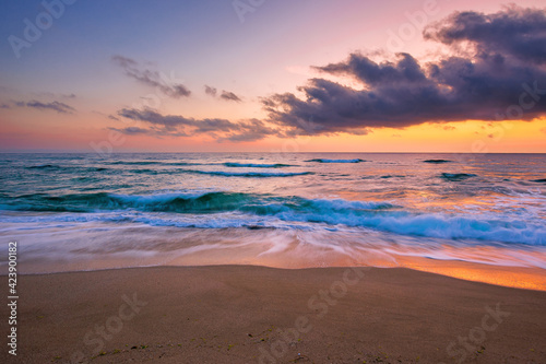 ocean beach with dramatic sky at sunrise. gorgeous vacation scenery. waves rolling on the sand in morning light © Pellinni