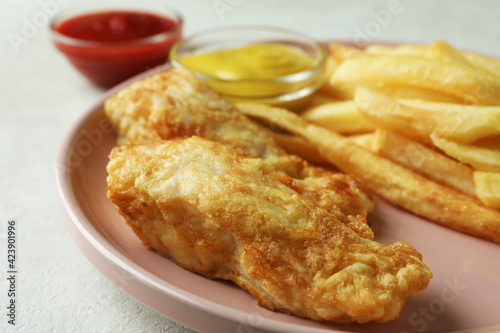 Plate with fried fish and chips, and sauces on white textured background