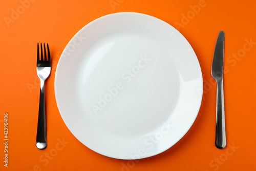 Plate with chocolate piece and cutlery on orange background