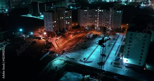 Night aerial shoot of flying above constructor crane in mysterious modern town. Unusual cool colors creating suspense atmosphere