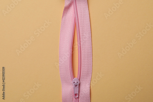 Pink zipper on beige background, close up