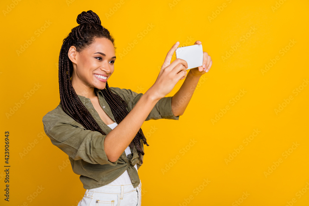 Photo portrait of woman photographing holding phone vertically in two hands isolated on vivid yellow colored background