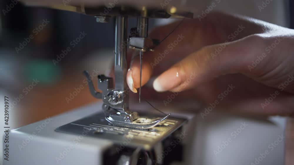 Female hands put black thread into the needle of the sewing machine close-up. Textile industry concept. Female hands put black thread into the needle of the sewing machine close-up. Textile industry concept.
