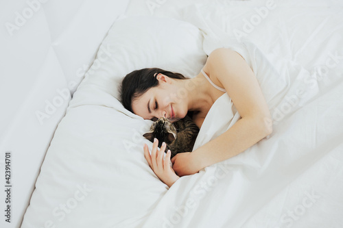 Beautiful young smiling woman with cute cat lying in bed at home.