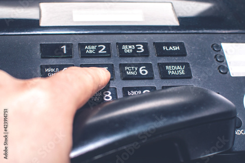 The hand of an office worker holds the phone receiver and presses the keys