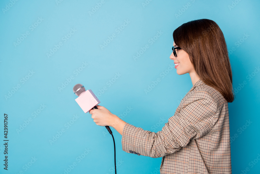 Photo portrait side profile of woman holding microphone with blank space isolated on vivid blue colored background Photo portrait side profile of woman holding microphone with blank space isolated on vivid blue colored background