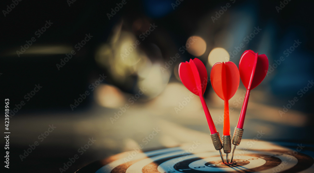 Fototapeta premium Close up shot of the dart arrow hit on bulleyes of dartboard to represent that the business reached the target with dark tone picture style. Target and goal as concept.