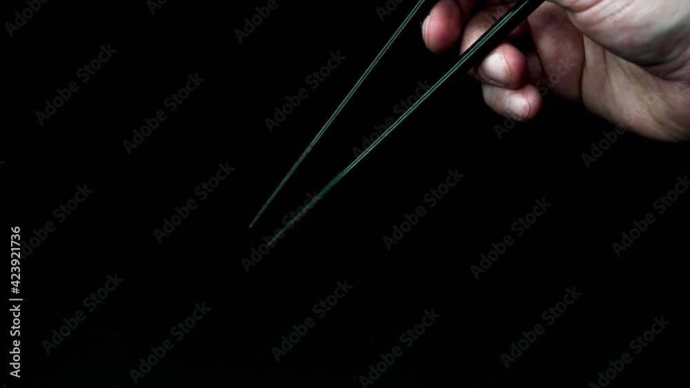 one hand moves two black chopsticks in the typical posture against a black background slow motion one hand moves two black chopsticks in the typical posture against a black background slow motion