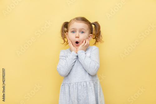 Wow. Closeup portrait of excited child touching her cheeks, over pastel yellow isolated background.The concept of advertising goods, seasonal sale, discount. Shopping and retail. Promoting goods