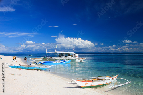 wooden boats on the sandy beach at crystal clear blue waters with blue sky in the back at the tropical island Malapascua in the Philippines photo