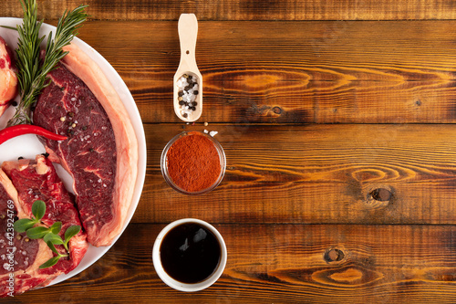 Chunks of raw meat on a white plate. Wooden table. Sauce, spises. Copy space. photo