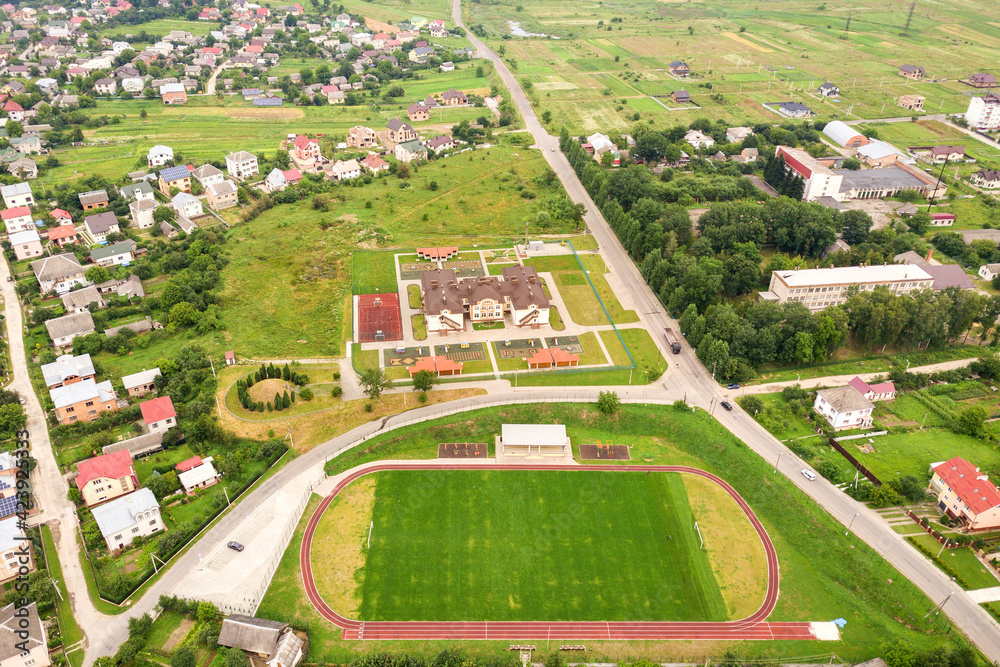 Aerial view of sports stadium with red running tracks and green grass football field near school building in rural area. Aerial view of sports stadium with red running tracks and green grass football field near school building in rural area.