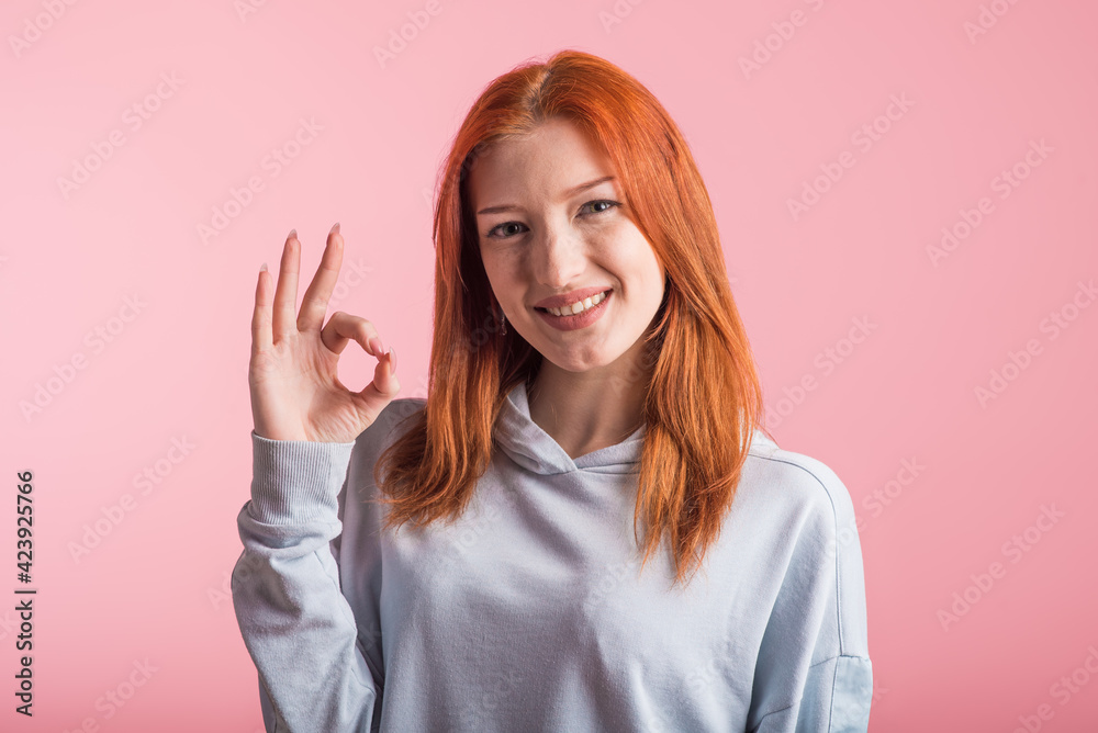Redhead girl showing Okay gesture in studio on pink background Redhead girl showing Okay gesture in studio on pink background