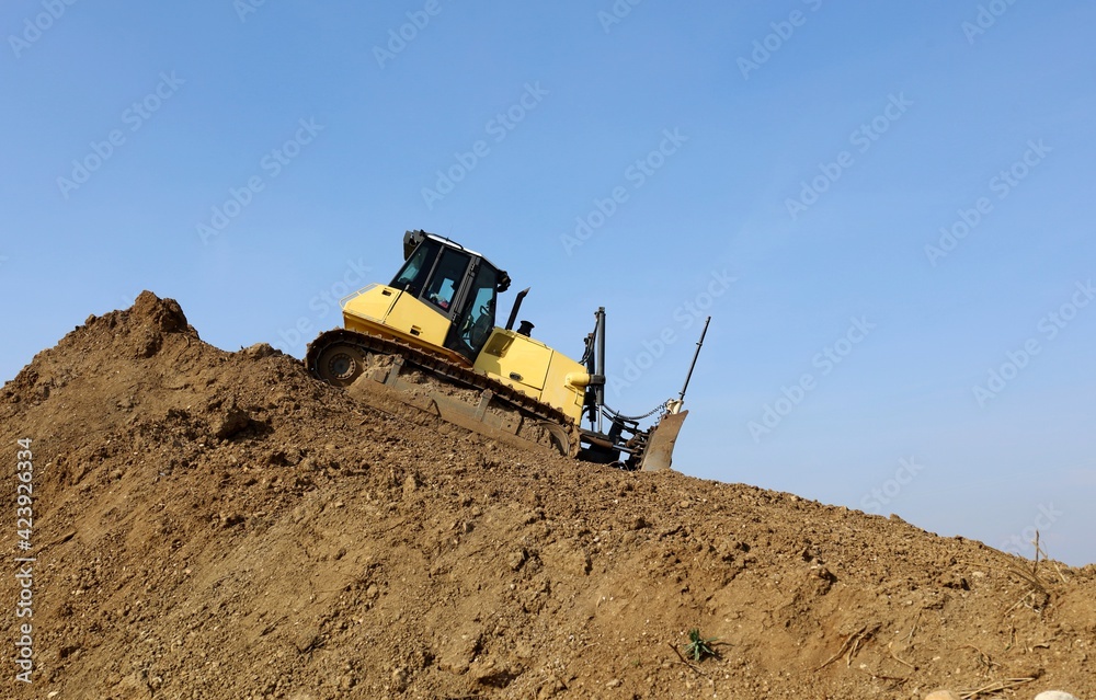 Bulldozer at work on the descent of a large pile of dirt. Side view. Bulldozer at work on the descent of a large pile of dirt. Side view.