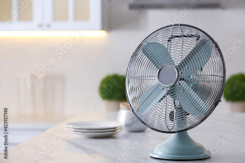 Modern electric fan on countertop in kitchen, space for text. Summer heat