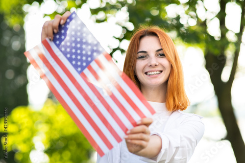 Happy young woman posing with USA national flag outdoors in summer park. Pretty girl celebrating United States independence day. photo