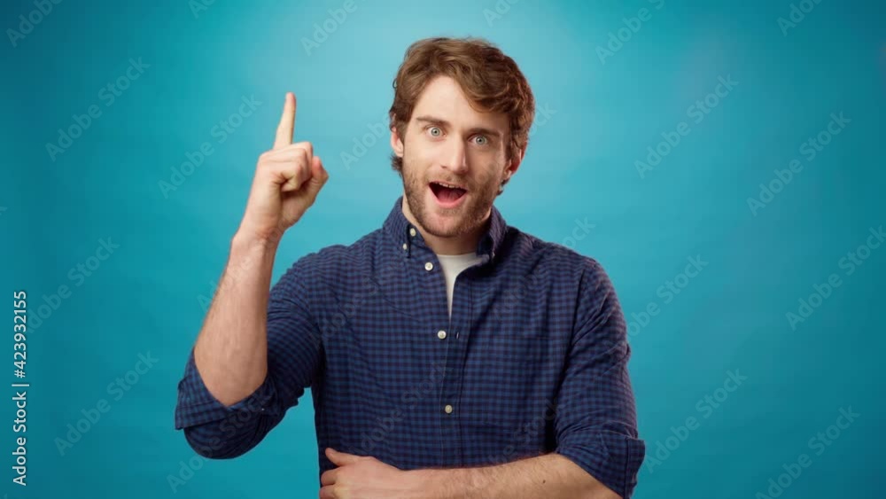Thoughtful young man has an idea, pointing up, blue background