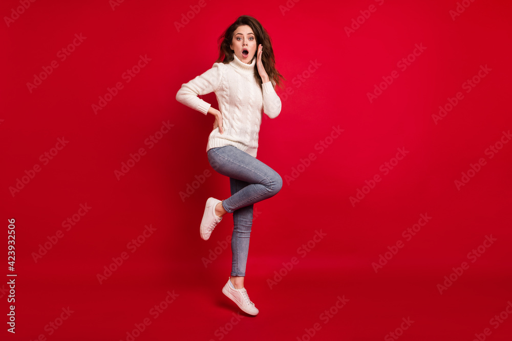 Full length photo of impressed pretty young woman dressed white sweater jumping high arm cheek isolated red color background