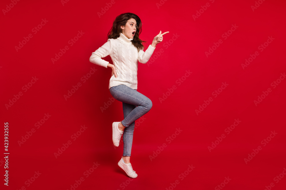 Full length photo of cute excited lady wear collar pullover pointing finger empty space jumping high isolated red color background