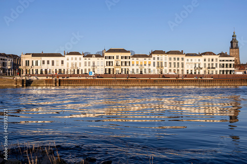 Cityscape countenance of historic Hanseatic Zutphen, The Netherlands, reflecting in the river IJssel seen from the opposite shore at sunset against a clear blue sky © Maarten Zeehandelaar