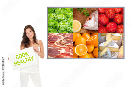 Beautiful young women wearing white sportswear and holding a sign in front of a photo with colorful food, cook healthy is written on the papers, isolated on white background photo