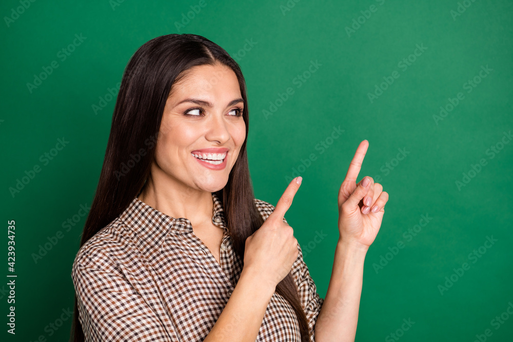 Photo of charming lady direct forefingers look empty space wear checkered shirt isolated green color background Photo of charming lady direct forefingers look empty space wear checkered shirt isolated green color background