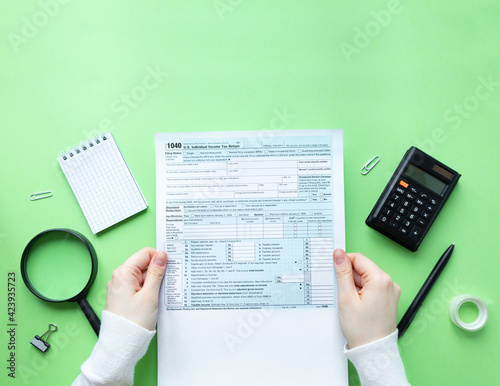 A man holds a 1040 tax form in his hands. Filling out taxation documents. Green background with copy space