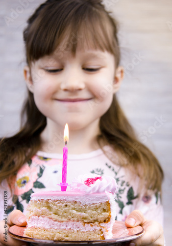 the girl holds a birthday cake with a candle in her hands and smiles