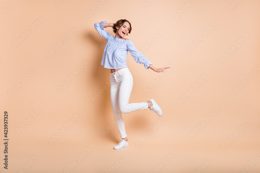 Full length photo of young excited girl happy positive smile have fun dance look empty space isolated over beige color background