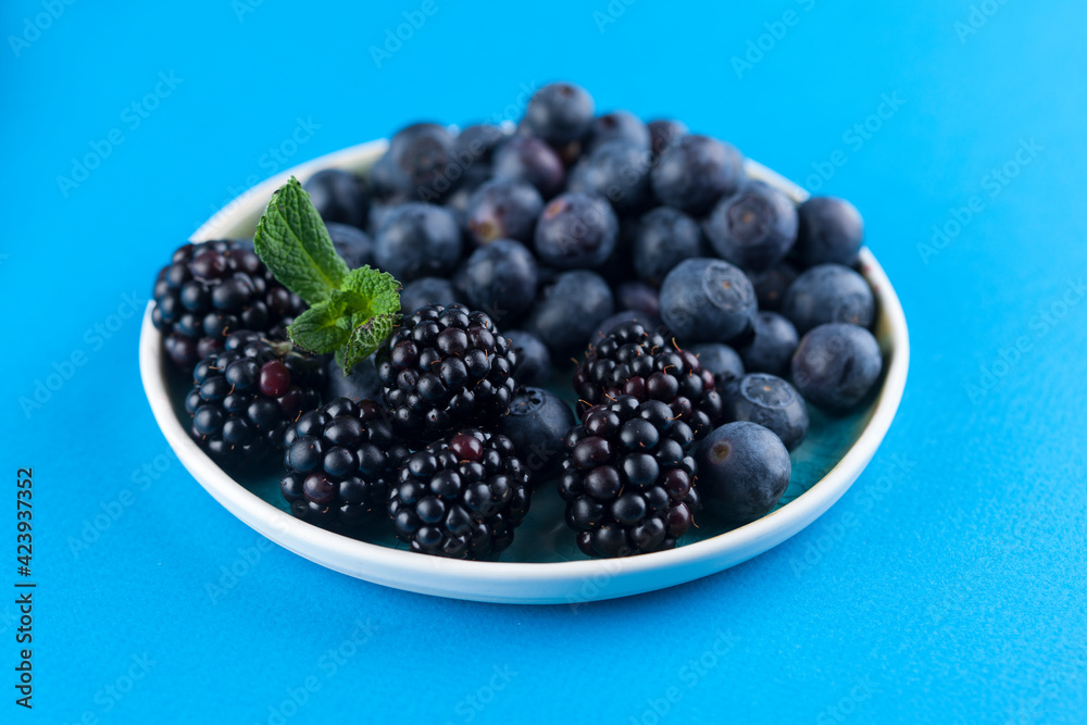 Food Photography - Blueberries and blackberries on a blue artisan plate against a blue background with mint leaves Food Photography - Blueberries and blackberries on a blue artisan plate against a blue background with mint leaves