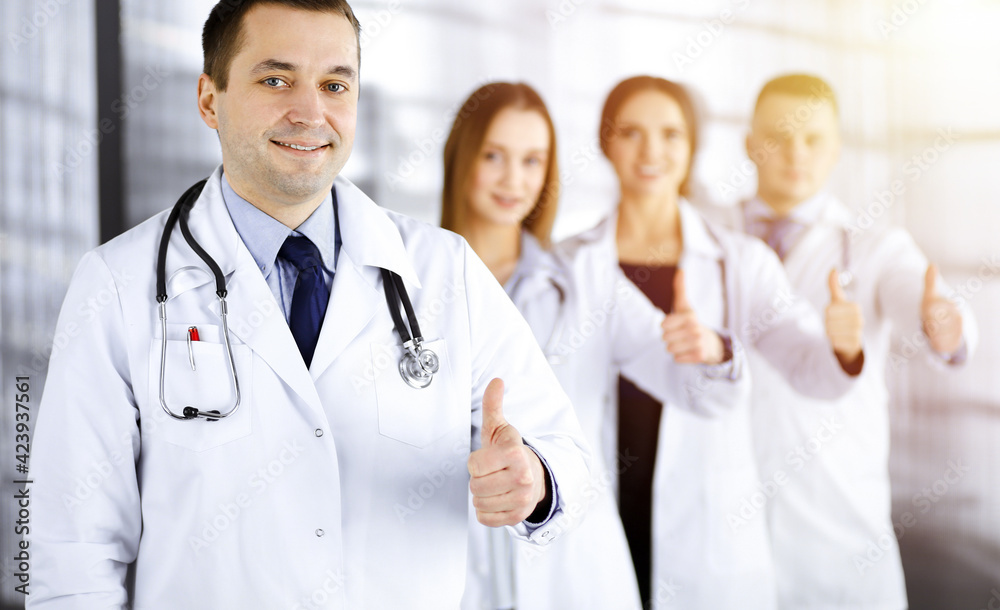 Group of professional doctors are standing as a team with thumbs up in a sunny hospital office, ready to help their patients. Best medical help, insurance in health care and medicine concept Group of professional doctors are standing as a team with thumbs up in a sunny hospital office, ready to help their patients. Best medical help, insurance in health care and medicine concept