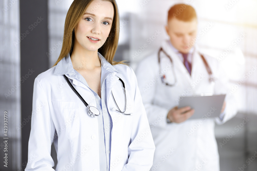 Professional beautiful woman-doctor with a stethoscope is standing with crossed arms in a sunny clinic. Young doctors at work in a hospital. Perfect medicine concept Professional beautiful woman-doctor with a stethoscope is standing with crossed arms in a sunny clinic. Young doctors at work in a hospital. Perfect medicine concept