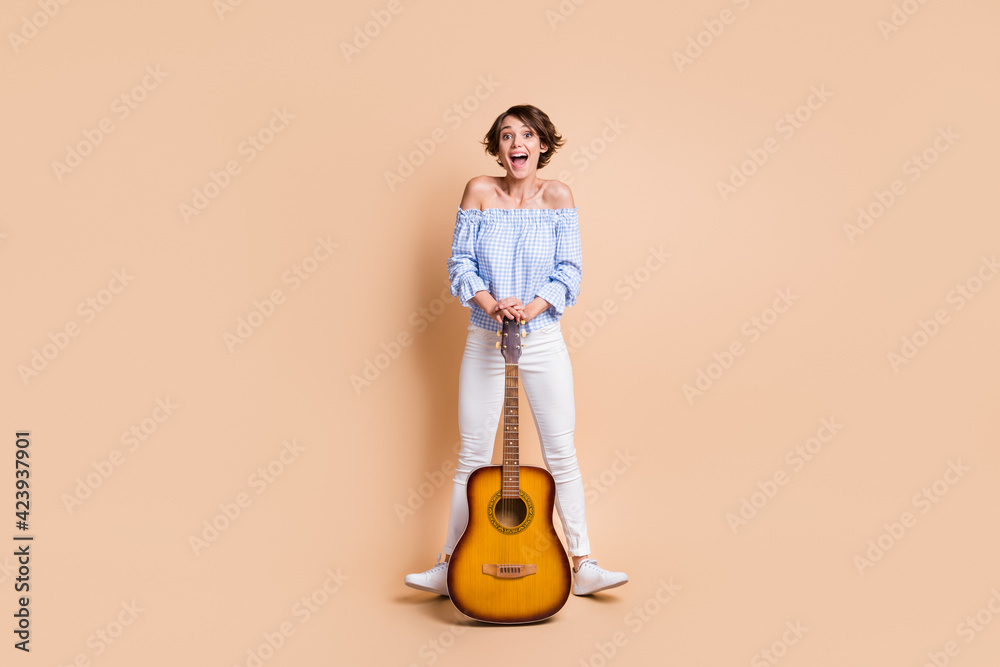 Full body photo of young cheerful excited girl happy positive smile guitar artist isolated over beige color background Full body photo of young cheerful excited girl happy positive smile guitar artist isolated over beige color background
