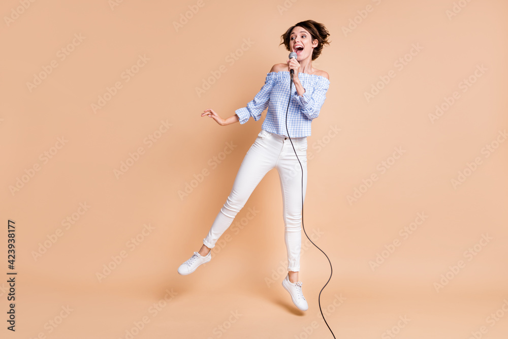 Full length body size view of lovely talented cheerful girl jumping singing having fun isolated over beige pastel color background Full length body size view of lovely talented cheerful girl jumping singing having fun isolated over beige pastel color background