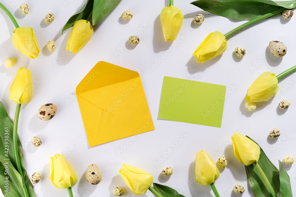 Colorful easter quail eggs and tulips with envelope on white background . Flat lay.