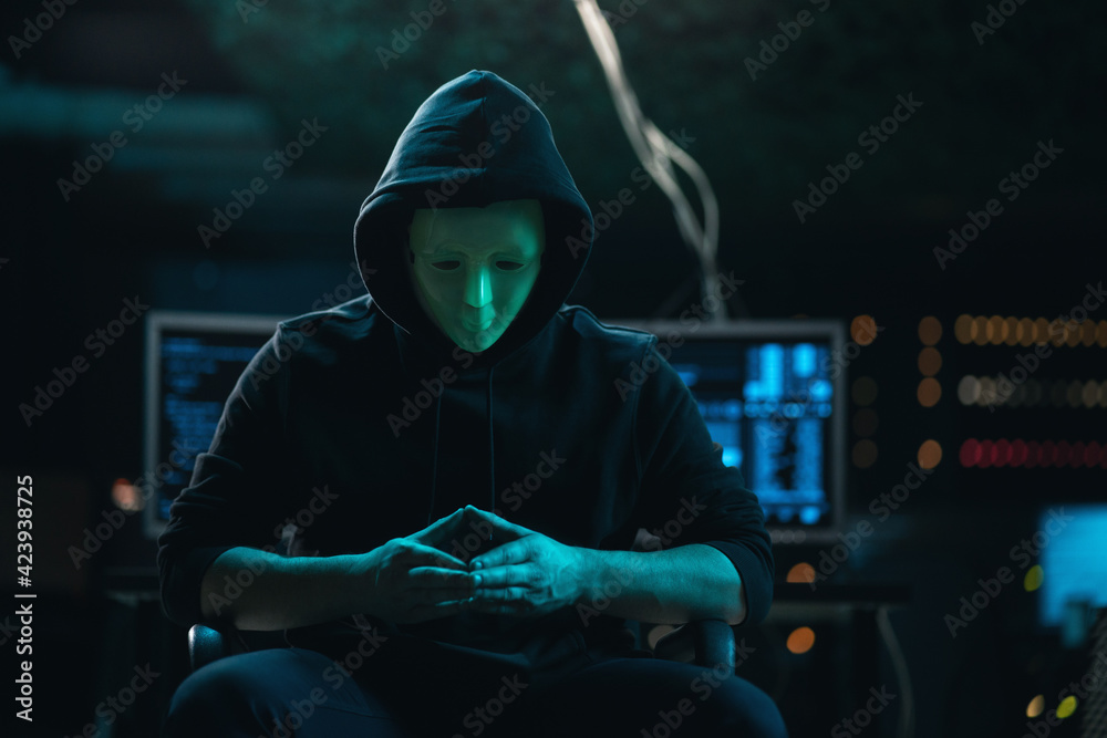 Close-up Shot of Masked Anonymous Hacker Organizes malware Attack on Global Scale. He is in Underground Secret Location Surrounded by Displays and Cables. Close-up Shot of Masked Anonymous Hacker Organizes malware Attack on Global Scale. He is in Underground Secret Location Surrounded by Displays and Cables.
