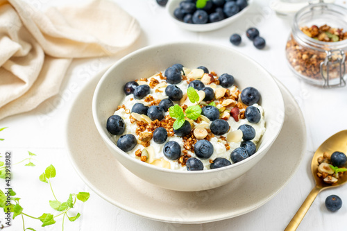 Yogurt with muesli, nuts and blueberries in a ceramic plate on the white kitchen table. Soft cream cheese with muesli and berries in a bowl closeup. Healthy Breakfast Concept