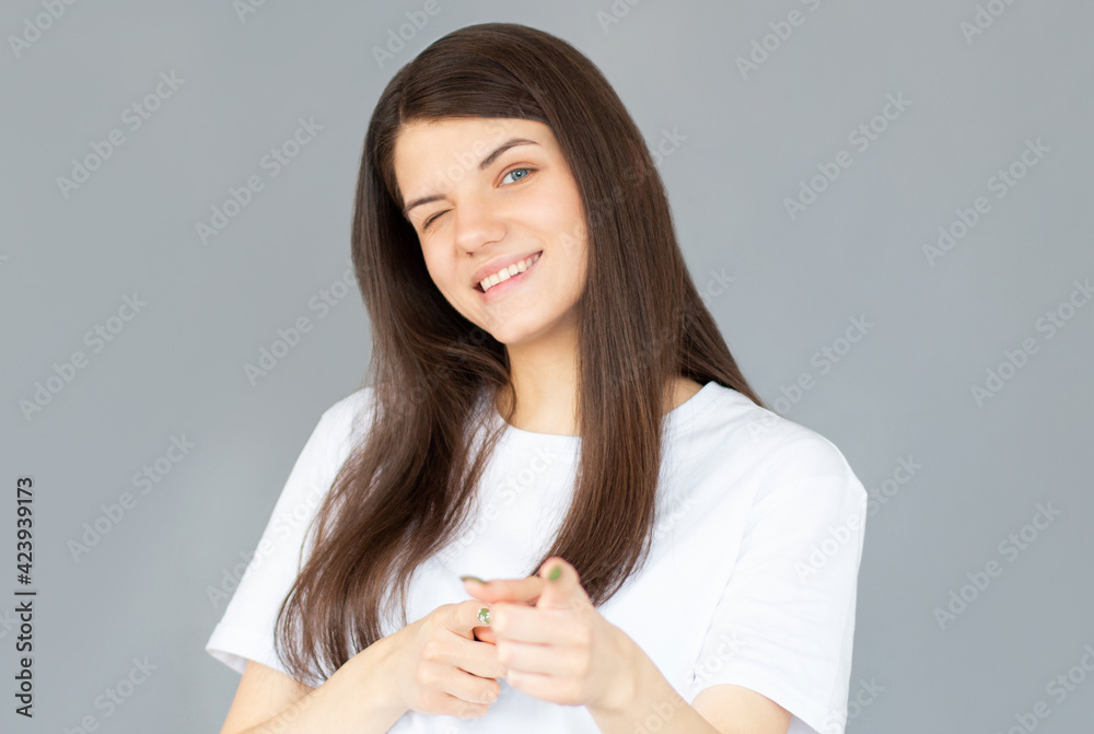 Smiling happy woman pointing at the camera with both hands and her head tilted to the side with a playful expression and focus to her face over grey Smiling happy woman pointing at the camera with both hands and her head tilted to the side with a playful expression and focus to her face over grey
