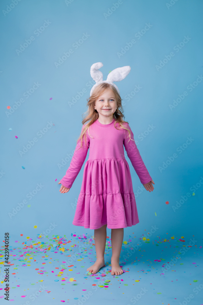 Cute little blonde girl in Easter bunny ears in pink dress on a blue background. Easter concept, text space Cute little blonde girl in Easter bunny ears in pink dress on a blue background. Easter concept, text space