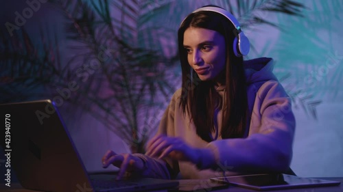 Female working with headphones, a tablet and a laptop on a colorful neon light background. Close-up.