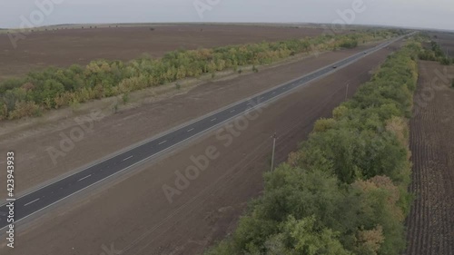 The copter flies over the road, to the left and right of it is a field and a forest, a car is driving along the road