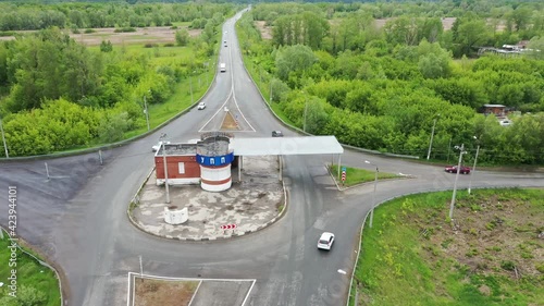 The copter flies over the road, to the left and right of it is a field and a forest, a car is driving along the road