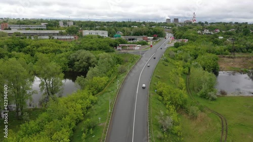 the quadcopter flies over the road, the entrance to the city, to the right of the road is a lake, on the horizon you can see the factory