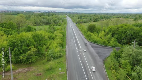 The copter flies over the road, to the left and right of it is a field and a forest, a car is driving along the road