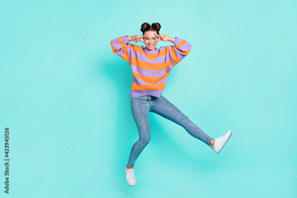 Full length body size view of lovely trendy cheerful girl jumping showing v-sign having fun isolated over bright teal turquoise color background Full length body size view of lovely trendy cheerful girl jumping showing v-sign having fun isolated over bright teal turquoise color background